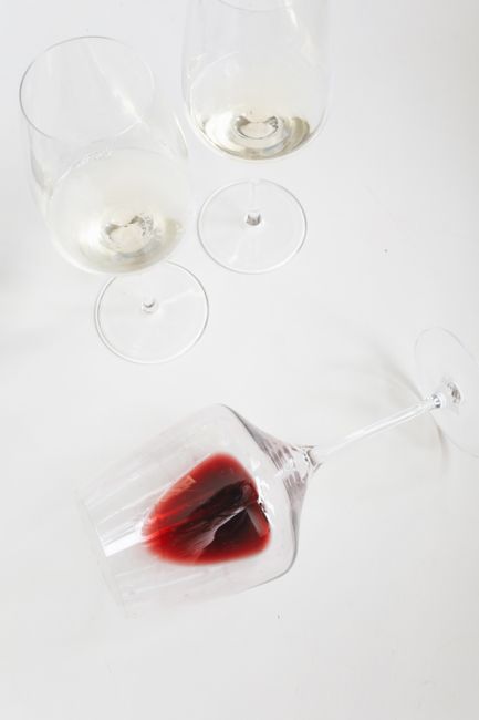 A close-up of a white fabric surface, likely a bedsheet or tablecloth, with a vivid red wine stain in the center. The fabric appears to be soft and slightly textured, with visible creases around the s